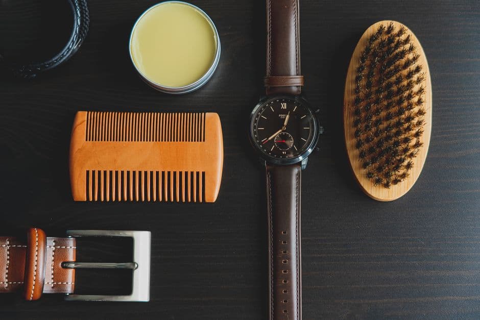 Flat lay of men's grooming accessories including watch, brush, comb, and pomade.